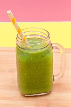 Fresh Green Smoothie of Apple, Celery, and Spinach in Glass Smoothie Jar with Yellow Cocktail Straw on Wooden Cutting Board. Vegan Detox Drink. Vegetarian Culture. Healthy Eating and Fruit Diet