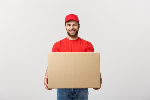 Young smiling logistic delivery man in red uniform holding the box on white background.