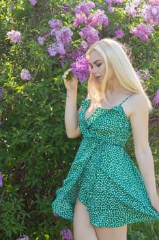 Fashionable girl model near a lilac bush. Spring flowers and beautiful blonde woman. Model appearance. Soft focus