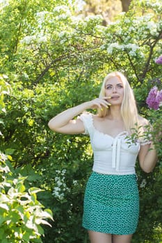 Fashionable girl model near a lilac bush. Spring flowers and beautiful blonde woman. Model appearance. Soft focus