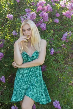 Fashionable girl model near a lilac bush. Spring flowers and beautiful blonde woman. Model appearance. Soft focus