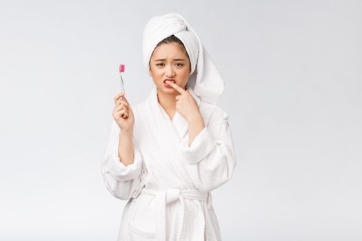 Unhappy beautiful woman brushing her teeth on white background.