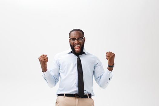 Happy african businessman wearing a corporate grey shirt and black tie punching the air with his fists arms in air, smiling and shouting in victorious success for his business deal.