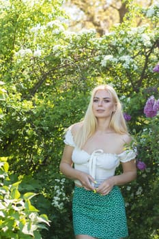 Fashionable girl model near a lilac bush. Spring flowers and beautiful blonde woman. Model appearance. Soft focus