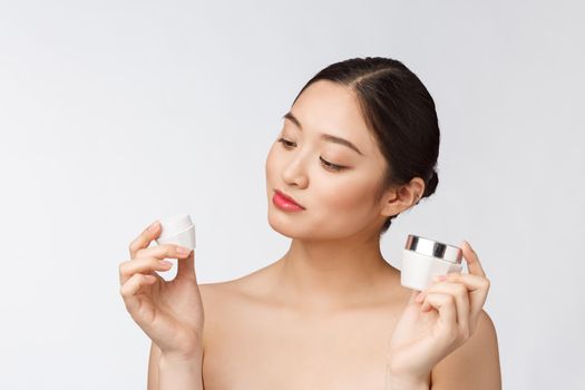 Beautiful young woman on white isolated background holding cosmetic face cream, asian.