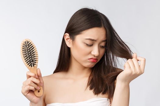 Upset stressed young Asian woman holding damaged dry hair on hands over white isolated background