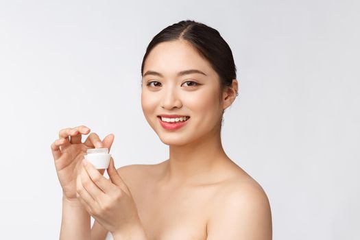 Beautiful young woman on white isolated background holding cosmetic face cream, asian.