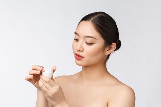 Beautiful young woman on white isolated background holding cosmetic face cream, asian.