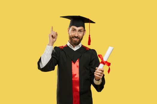 Front view of happy young man graduating from university, college. Boy with beard standing, smiling, raising finger, holding diploma, surprised. Concept of youth and knowledge.