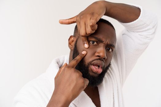 African American man looks at pimples on face. Acne. Male hygiene. Isolated on white background. Studio portrait.