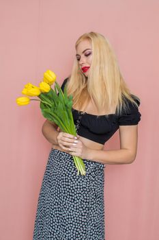 Summer fashion portrait blonde woman. Sexy look in black top and skirt. Red lips. Holding yellow tulips in her hands