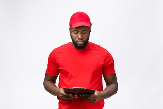 Thoughtful african american young delivery man writing on clipboard.