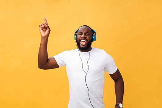 Young African American man wearing headphone and enjoy music dancing over yellow gold Background.