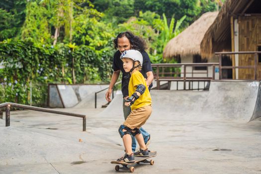 Athletic boy learns to skateboard with asian trainer in a skate park. Children education, sports. Race diversity.