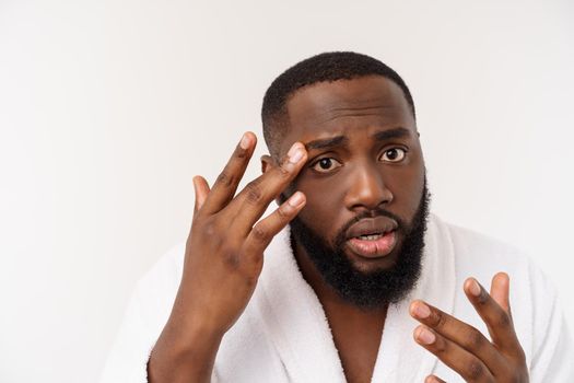 African American man looks at pimples on face. Acne. Male hygiene. Isolated on white background. Studio portrait.