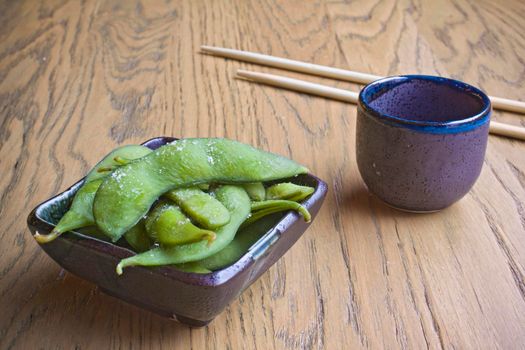 Edamame with sake and sushi chopstiks on a wooden table