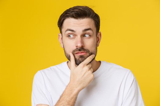 Thinking man isolated on yellow background. Closeup portrait of a casual young pensive man looking up at copyspace. Caucasian male model