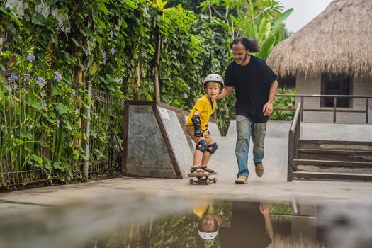 Athletic boy learns to skateboard with asian trainer in a skate park. Children education, sports. Race diversity.