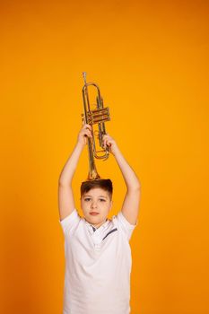 A boy in a white T-shirt holds a trumpet with a musical instrument on his head.