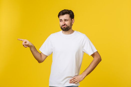 Handsome man over isolated yellow wall frustrated and pointing to the front