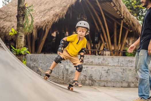 Athletic boy learns to skateboard with a trainer in a skate park. Children education, sports.