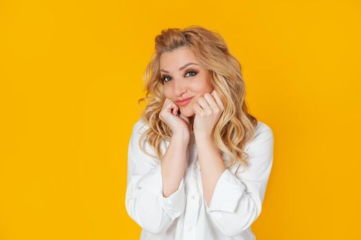 Cheerful, excited, sweet, happy, Caucasian blond woman, touches her cheeks. Smiling, having fun, waiting, standing joyfully, cannot wait impatiently to see the performance on a yellow background.