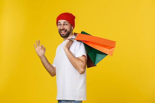 Photo of happy guy, holding shopping bags, isolated over yellow background.