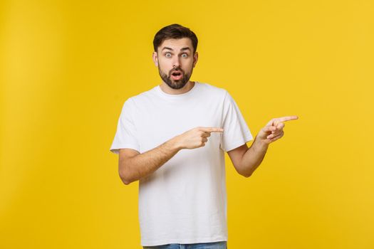 Man pointing showing copy space isolated on yellow background. Casual handsome Caucasian young man