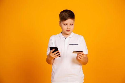 The boy pays with a credit card. Smiling teenage boy holding a credit card and smartphone, buying through the Internet