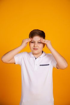 A boy with a headache. Caucasian child on a yellow background suffering from headache and migraine. Hands on the head.