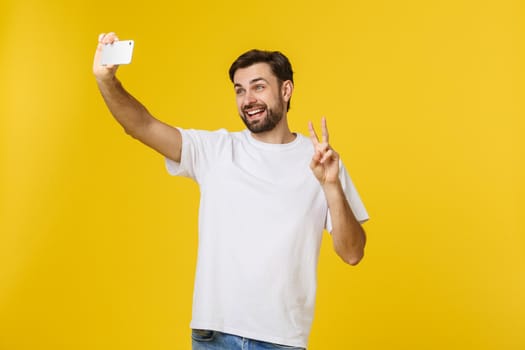 Closeup of young handsome man looking at smartphone and taking selfie. isolate over yellow background