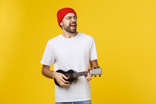 close-up of funny young man playing a guitar. isolated on yellow gold background.