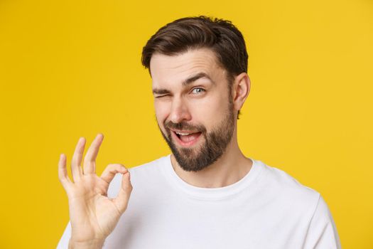 Satisfied young man showing okay sign isolated on yellow background