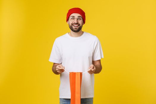 Full isolated studio picture from a young man opening shopping bags. Isolate over yellow background