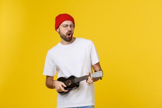 close-up of funny young man playing a guitar. isolated on yellow gold background.