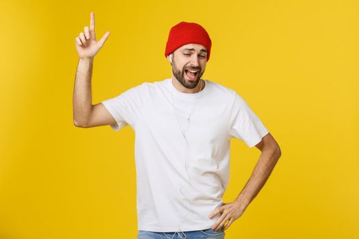 Portrait of a handsome young man dancing and listening music, isolated on yellow background.