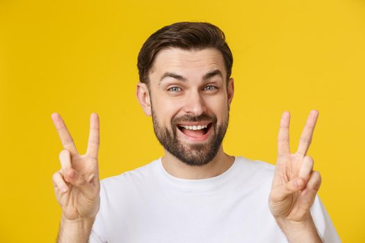 Young handsome man wearing striped t-shirt over isolated yellow background smiling looking to the camera showing fingers doing victory sign. Number two.