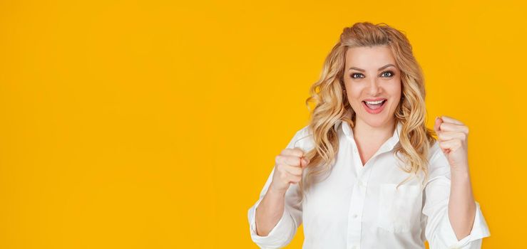 Cheerful, happy woman raising her hands with her fist, cheering for the team, winning a huge bet, playing in the casino in delight, cheering friends, watching football, yellow background