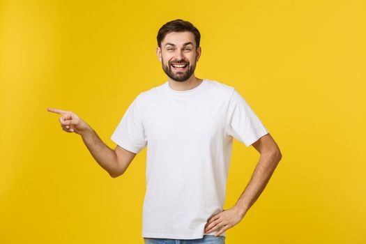 Man pointing showing copy space isolated on yellow background. Casual handsome Caucasian young man