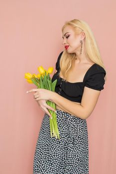 Summer fashion portrait blonde woman. Sexy look in black top and skirt. Red lips. Holding yellow tulips in her hands