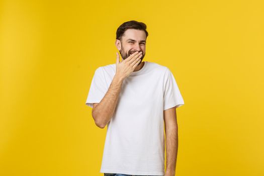 Close up portrait of young man laughing with hand covering mouth by yellow background.
