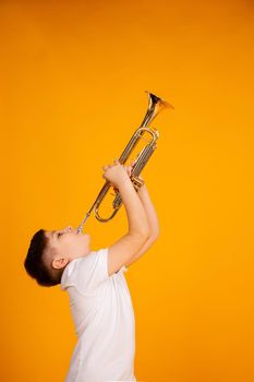 A boy plays the trumpet. A handsome teenager boy in a white T-shirt plays trumpet musical instrument