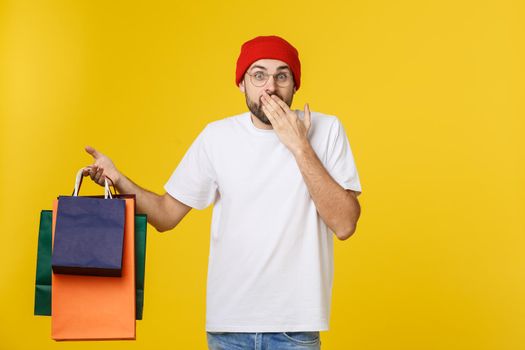 Bearded man with shopping bags with happy feeling isolated on yellow bacground.