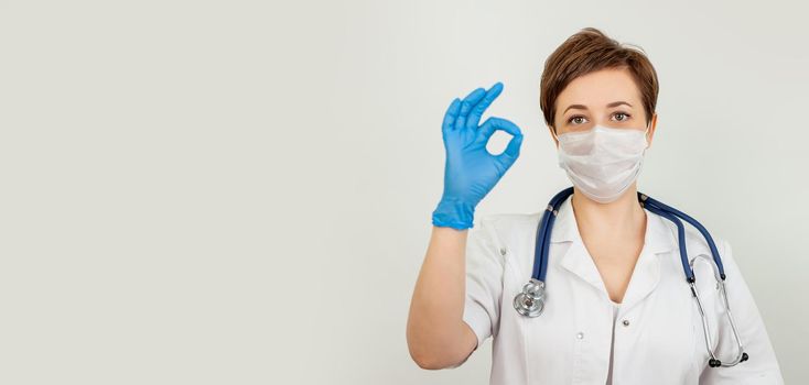 Young woman nurse or physician wearing a medical face mask, studio portrait. A health worker wearing a protective mask and showing ok sign. Woman wears a surgical mask for the crown virus