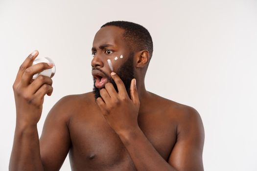 African handsome man applying cream on his face. Man's skin care concept.