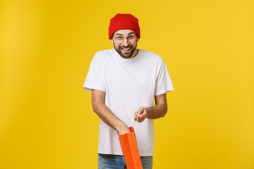 Full isolated studio picture from a young man opening shopping bags. Isolate over yellow background