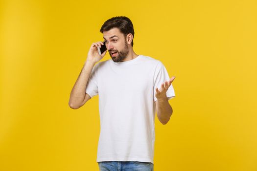 Portrait of a serious man talking on the phone isolated on a yellow background. Looking at camera.