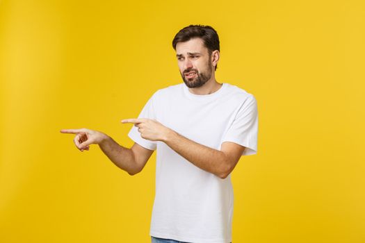 Handsome man over isolated yellow wall frustrated and pointing to the front