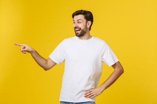 Man pointing showing copy space isolated on yellow background. Casual handsome Caucasian young man