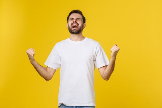 Happy young man with arms up isolated on a yellow background